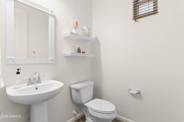 half bathroom featuring baseboards, a sink, and toilet