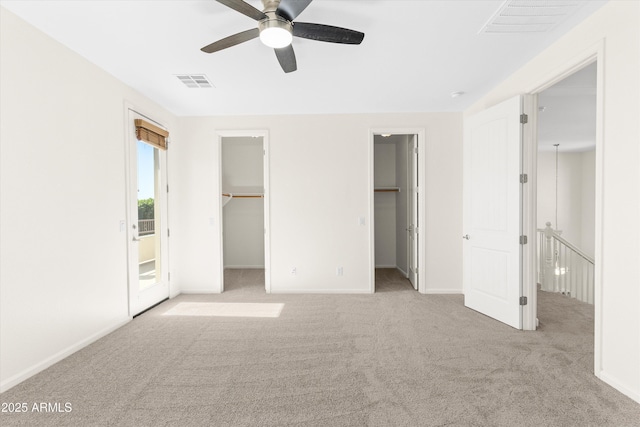 unfurnished bedroom featuring carpet floors, a walk in closet, visible vents, ceiling fan, and baseboards