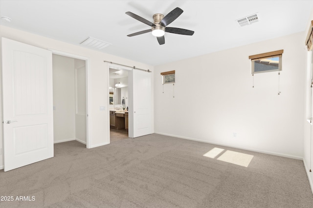 unfurnished bedroom featuring carpet, a barn door, visible vents, and baseboards