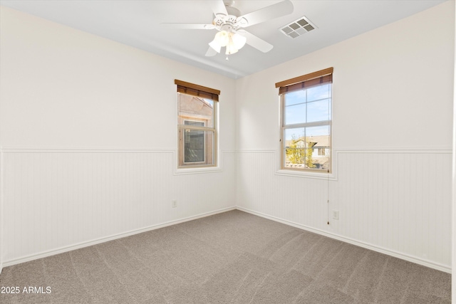 carpeted spare room featuring a wainscoted wall, ceiling fan, and visible vents