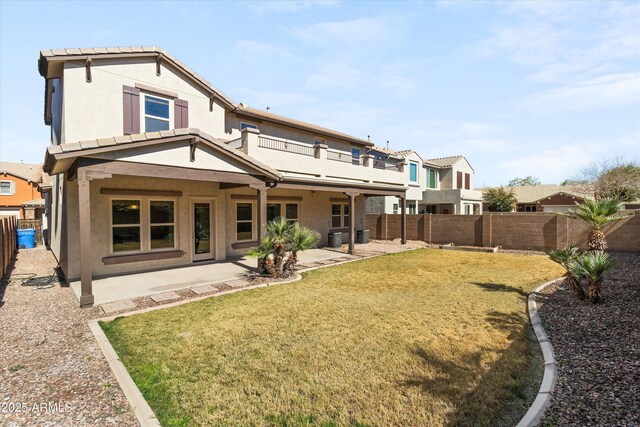 back of property featuring a fenced backyard, a balcony, a lawn, stucco siding, and a patio area