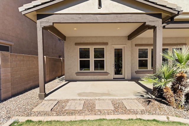 view of exterior entry with a patio area, fence, and stucco siding