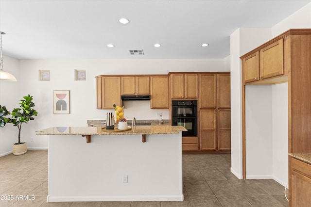 kitchen featuring under cabinet range hood, light stone countertops, visible vents, and dobule oven black