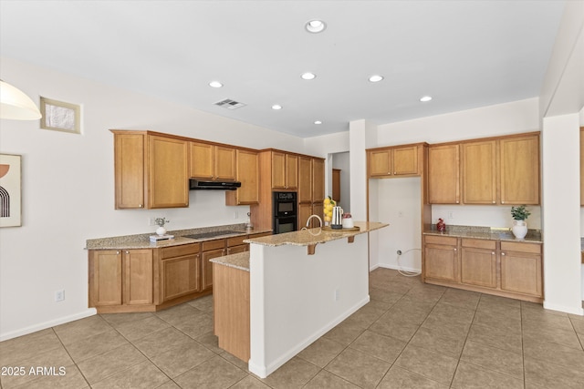 kitchen with black appliances, a kitchen island with sink, light stone counters, and brown cabinetry