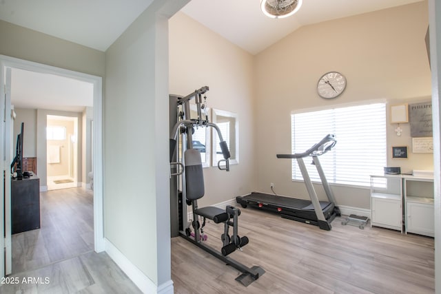 workout room featuring light wood-style floors, baseboards, and vaulted ceiling