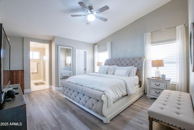 bedroom featuring lofted ceiling, light wood-style floors, baseboards, a ceiling fan, and ensuite bath