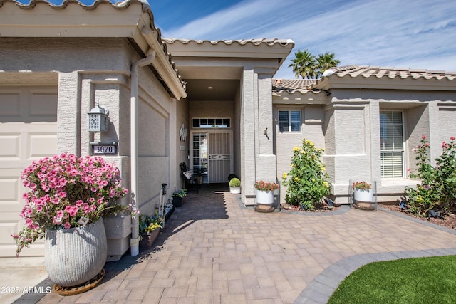 view of exterior entry featuring a garage, a tile roof, and stucco siding