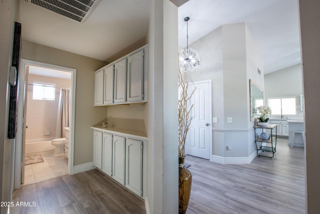hallway featuring a notable chandelier, baseboards, visible vents, and light wood-style floors