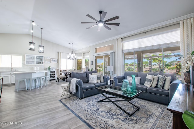 living area with plenty of natural light, light wood finished floors, ceiling fan with notable chandelier, and high vaulted ceiling