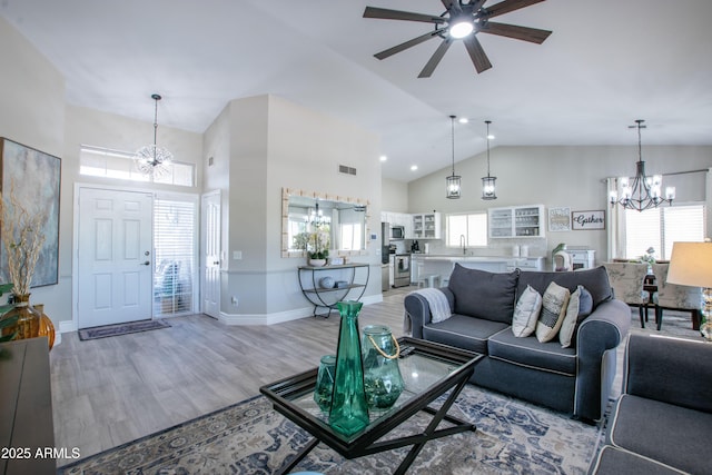 living room with a healthy amount of sunlight, visible vents, high vaulted ceiling, ceiling fan with notable chandelier, and light wood-style flooring