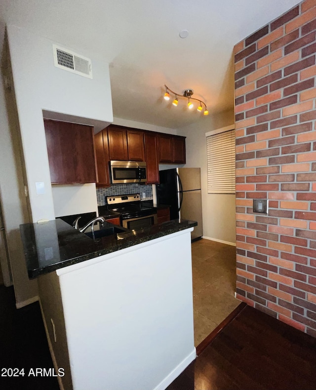 kitchen with kitchen peninsula, backsplash, dark stone counters, stainless steel appliances, and dark wood-type flooring