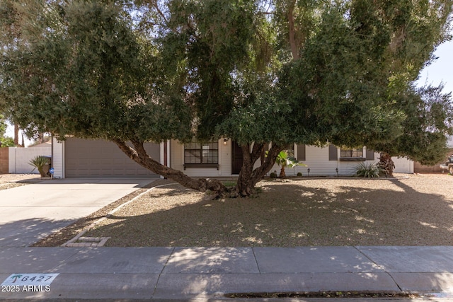 view of property hidden behind natural elements featuring a garage, fence, and concrete driveway