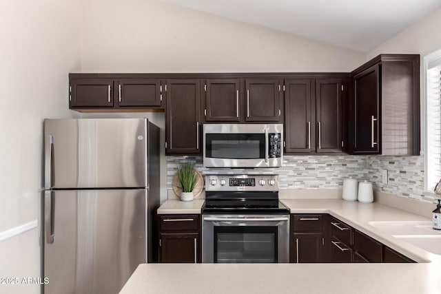 kitchen with dark brown cabinetry, vaulted ceiling, light countertops, appliances with stainless steel finishes, and backsplash