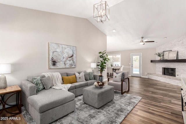 living area featuring baseboards, wood finished floors, vaulted ceiling, a fireplace, and ceiling fan with notable chandelier