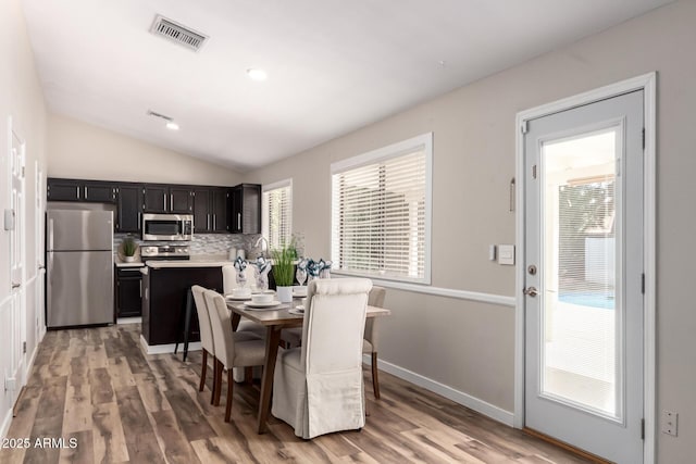 dining space with light wood-style floors, a wealth of natural light, visible vents, and vaulted ceiling