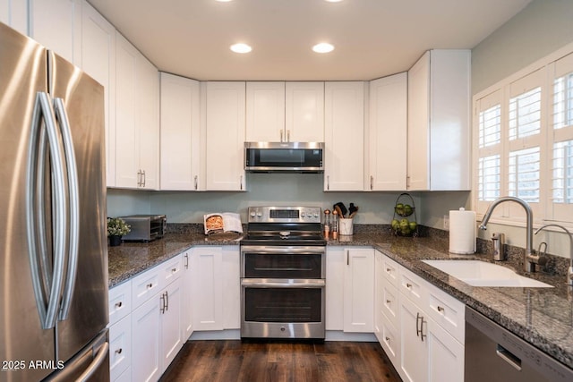 kitchen featuring dark stone countertops, stainless steel appliances, sink, and white cabinets