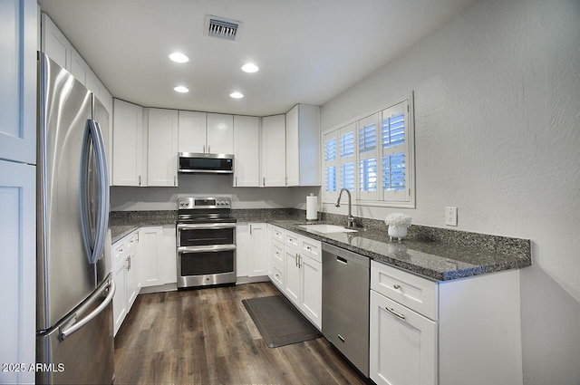 kitchen featuring sink, dark wood-type flooring, appliances with stainless steel finishes, dark stone countertops, and white cabinets