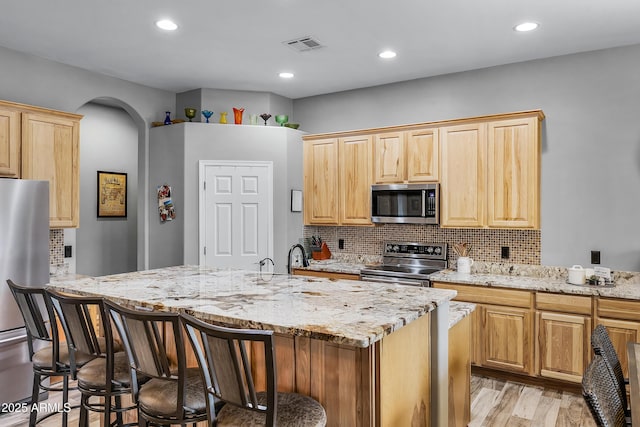 kitchen with appliances with stainless steel finishes, a kitchen breakfast bar, light brown cabinetry, and light hardwood / wood-style floors