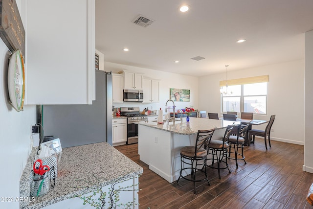 kitchen featuring hanging light fixtures, dark hardwood / wood-style flooring, an island with sink, white cabinets, and appliances with stainless steel finishes