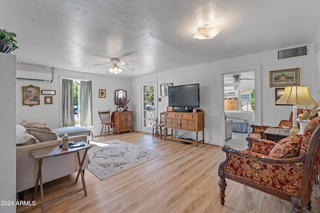 living room featuring light hardwood / wood-style floors, ceiling fan, and a wall unit AC