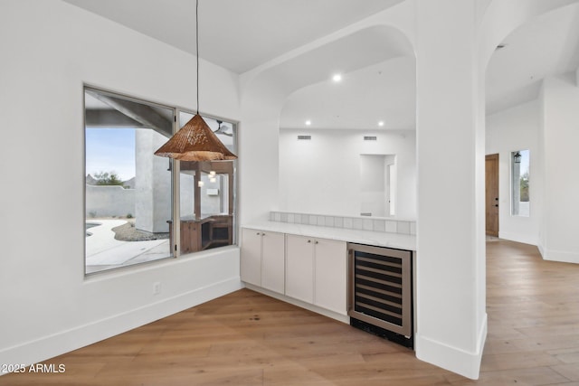 bar with beverage cooler, pendant lighting, baseboards, and light wood-style floors