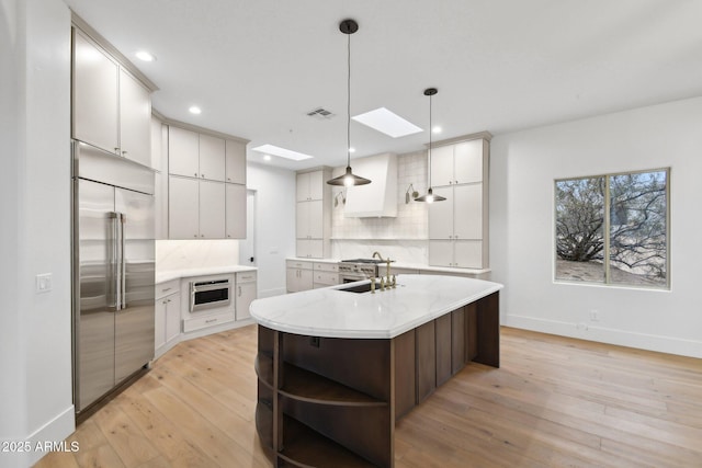 kitchen featuring visible vents, high end appliances, light countertops, light wood-style floors, and backsplash