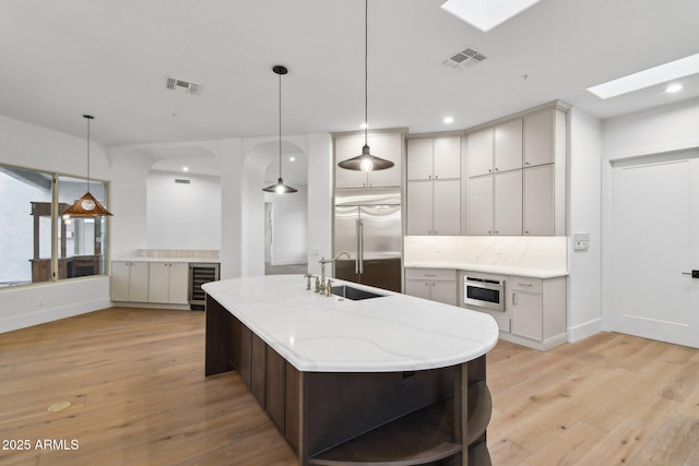 kitchen with a skylight, a sink, visible vents, light wood-type flooring, and stainless steel built in refrigerator