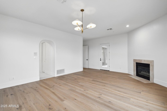 unfurnished living room with a fireplace with flush hearth, visible vents, a chandelier, and wood finished floors