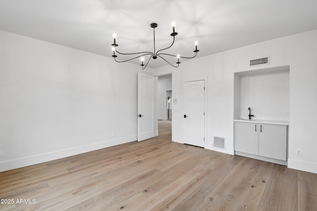 interior space featuring light wood-style floors, baseboards, visible vents, and a sink