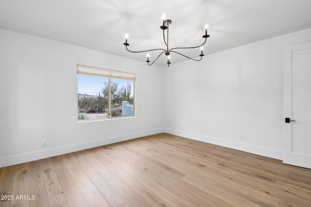 unfurnished room featuring light wood-style floors, baseboards, and an inviting chandelier