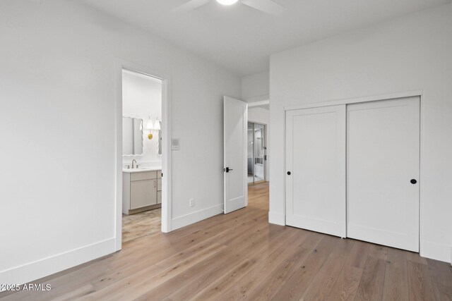 unfurnished bedroom with baseboards, light wood-style flooring, ensuite bathroom, a sink, and a closet