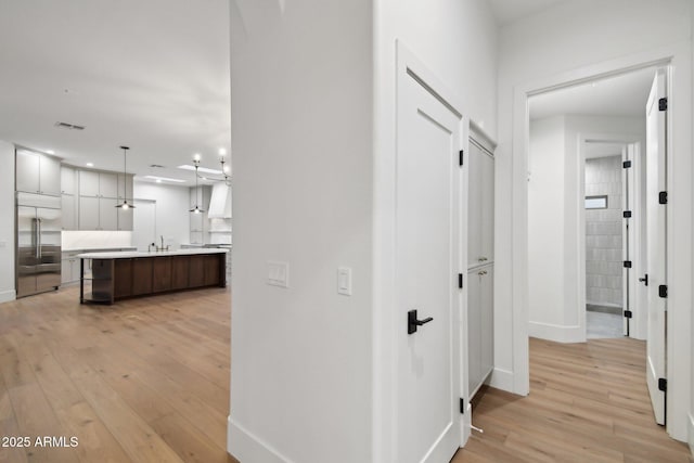 hall featuring light wood-type flooring, a sink, visible vents, and baseboards