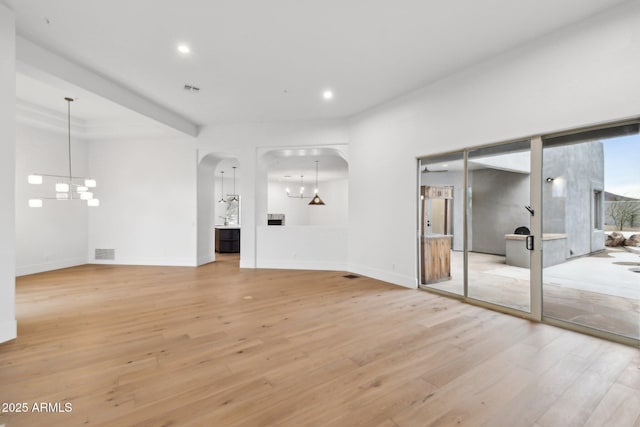 unfurnished living room featuring arched walkways, a notable chandelier, visible vents, light wood-style floors, and baseboards