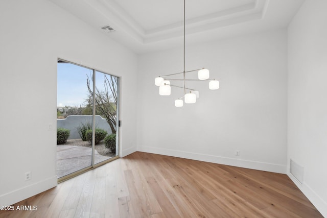 unfurnished dining area with a notable chandelier, baseboards, a raised ceiling, and wood finished floors