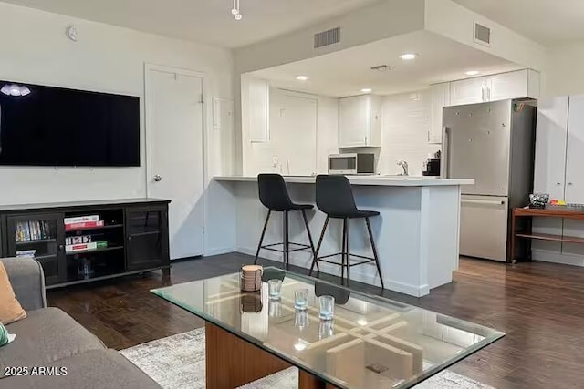 kitchen with a breakfast bar, appliances with stainless steel finishes, dark hardwood / wood-style floors, kitchen peninsula, and white cabinets