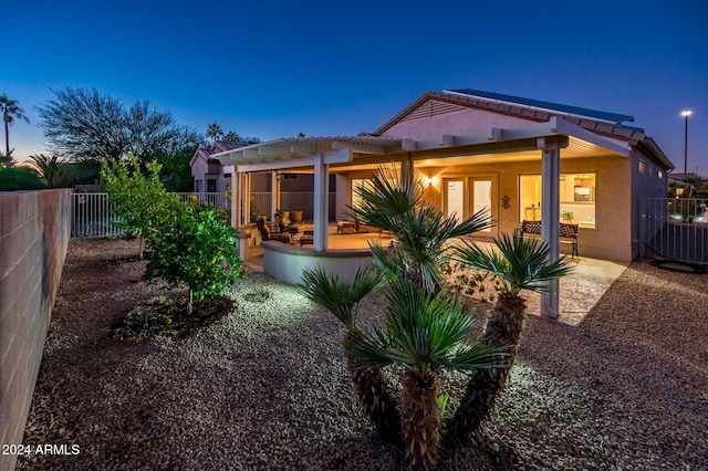 back house at dusk featuring a pergola and a patio area