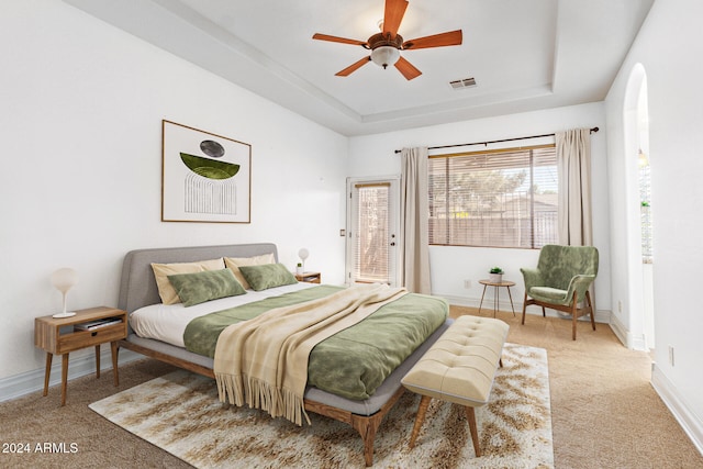 bedroom with a raised ceiling, ceiling fan, and light colored carpet