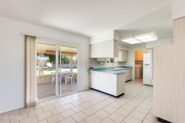 kitchen featuring washer / clothes dryer, white refrigerator with ice dispenser, sink, and white cabinets