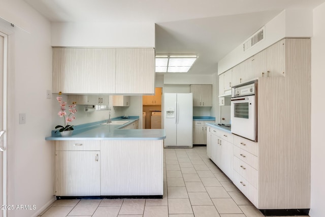 kitchen featuring white appliances, kitchen peninsula, sink, and light tile patterned floors