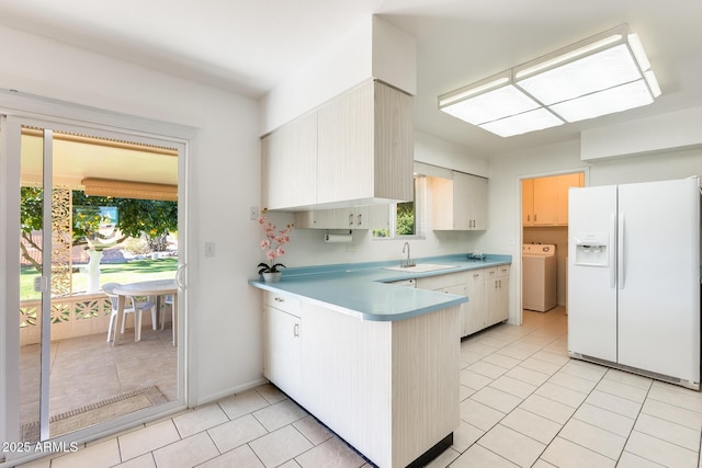 kitchen with sink, light tile patterned floors, white fridge with ice dispenser, washer / clothes dryer, and kitchen peninsula