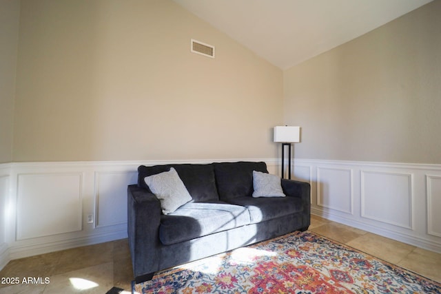living area with light tile patterned floors, visible vents, a decorative wall, a wainscoted wall, and vaulted ceiling
