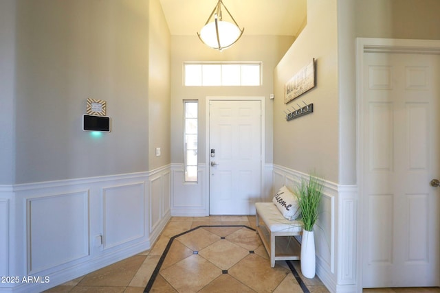 foyer entrance with wainscoting, a decorative wall, high vaulted ceiling, and light tile patterned floors