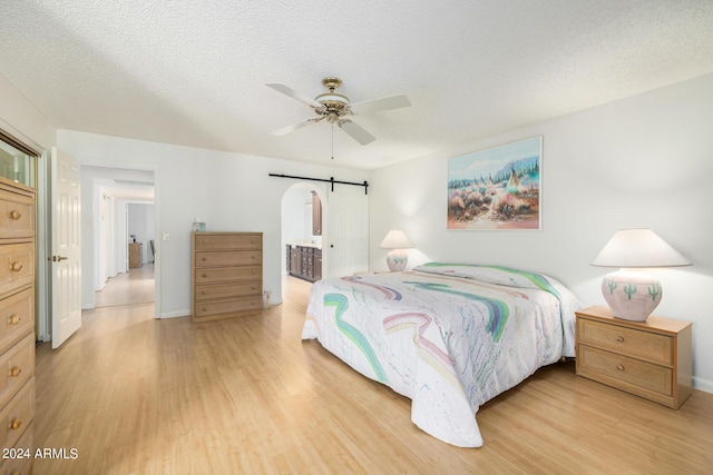 bedroom featuring a textured ceiling, light wood-type flooring, ensuite bath, and ceiling fan