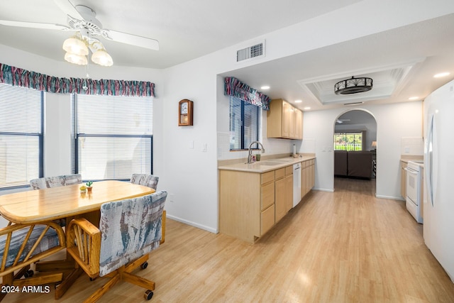 kitchen with light brown cabinets, sink, light hardwood / wood-style floors, white appliances, and a tray ceiling