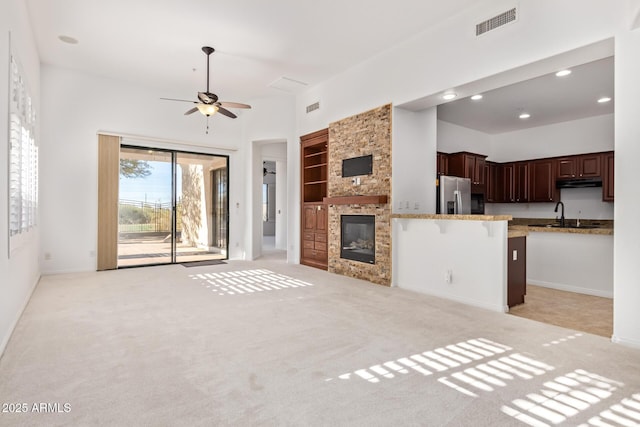 unfurnished living room with ceiling fan, sink, light carpet, and a stone fireplace