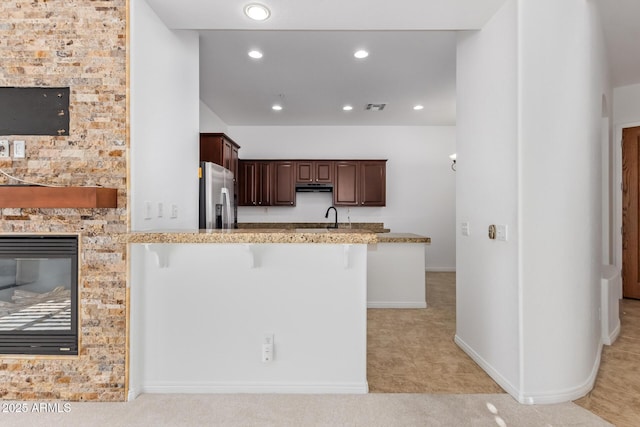 kitchen featuring stainless steel fridge with ice dispenser, kitchen peninsula, a fireplace, a breakfast bar, and sink