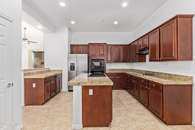 kitchen with black appliances, sink, a kitchen island with sink, ceiling fan, and light stone counters