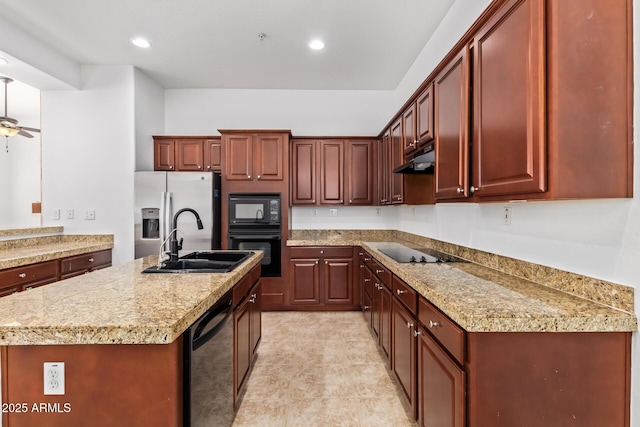 kitchen with light stone countertops, black appliances, sink, ceiling fan, and a center island with sink