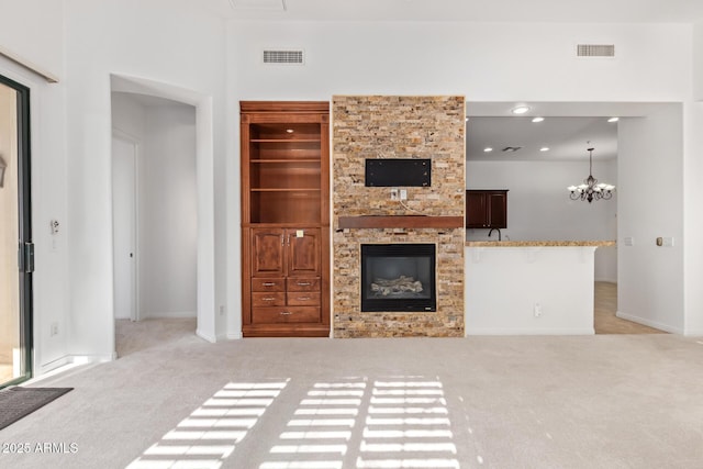 unfurnished living room featuring light colored carpet, built in shelves, a notable chandelier, and a stone fireplace