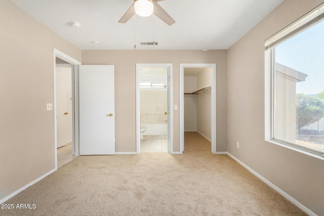 unfurnished bedroom with ensuite bath, a spacious closet, light colored carpet, a closet, and ceiling fan